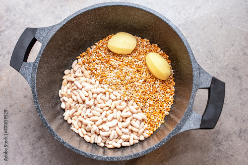 Top view of pot with potato, beans, wheat grains, pearl barley and spices in cooking pot on a grey marble kitchen table. Preparing winter food. photo