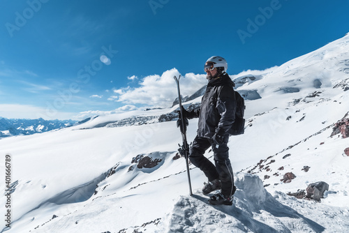 A man with skis stands high in the mountains enjoying the scenery. Go downhill skiing, extreme relaxation