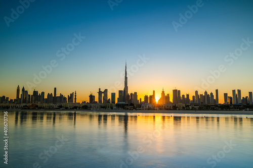 Sunrise in Dubai with clean blue sky view from boat or sea. The Sun rises over UAE skyscrapers at morning. Dubai beach  coast  shore