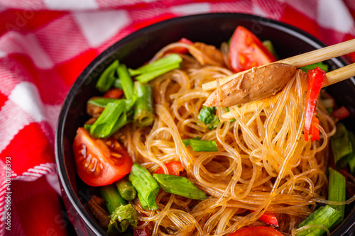 delicious glass noodles with chicken and vegetables on a dark stone background