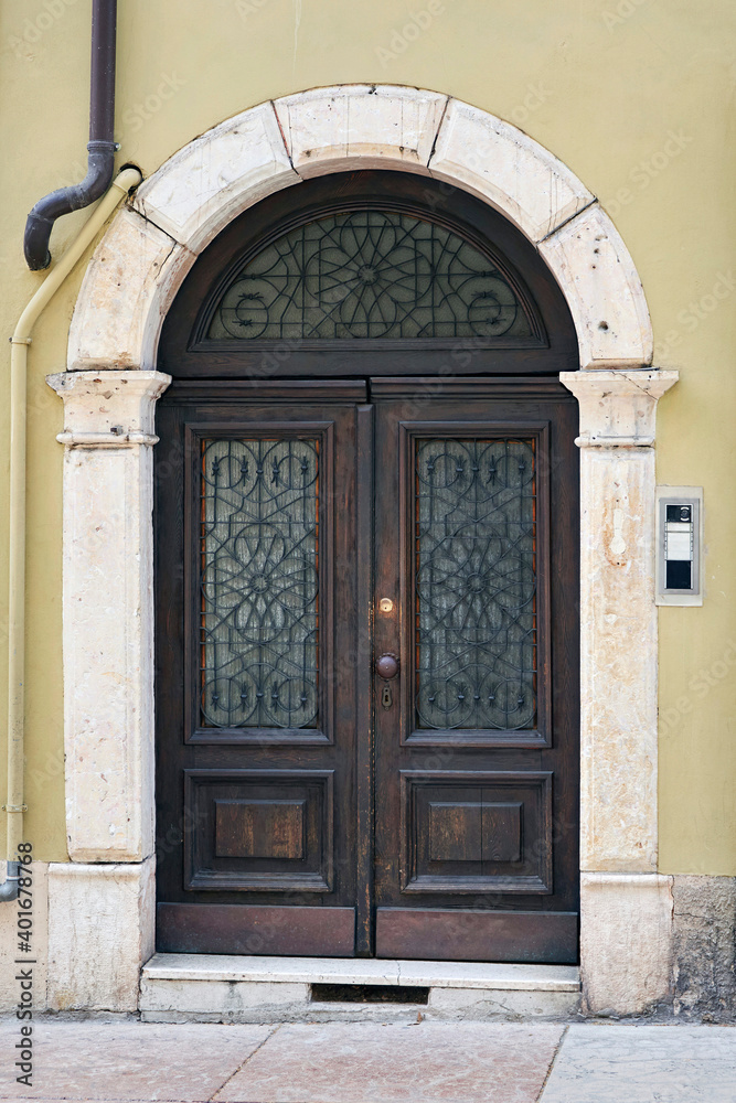 Italian retro wood style front door, the main entrance on the khaki color wall facade. Element of the classic Italian facade and architecture