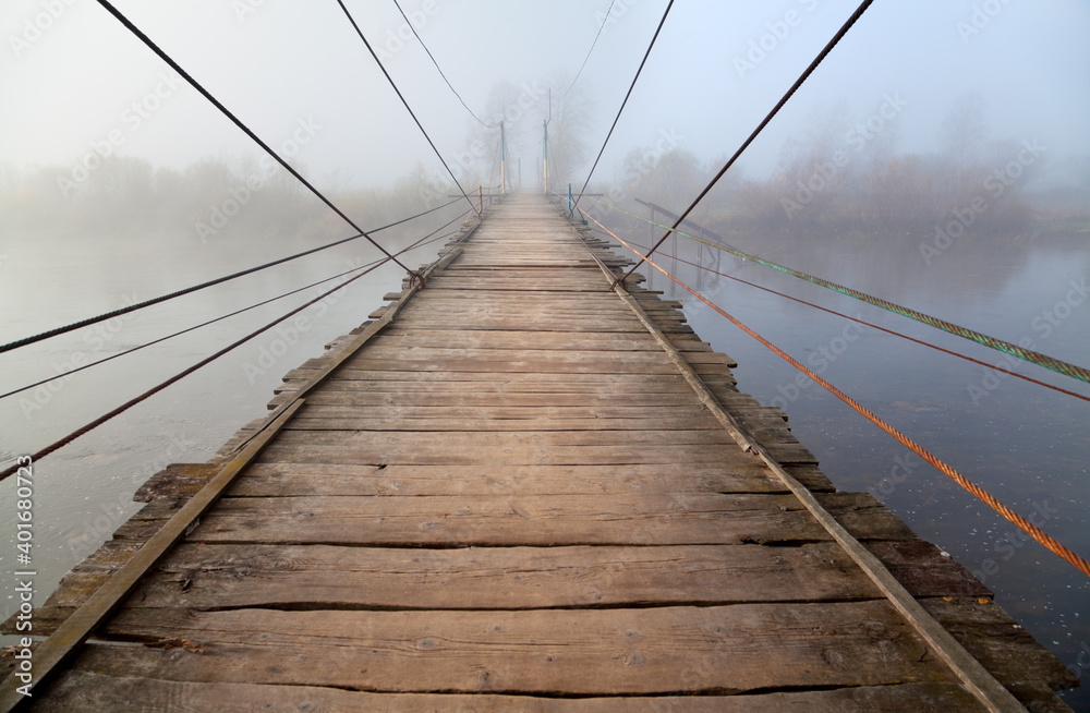 Wooden suspension bridge across river in deep fog. Ukraine, Carpathians.
