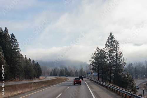 An asphalt road along which cars and trucks go, among the mountains, ahead on the horizon mountains in fog, the sky is covered with clouds. Idaho, USA, 11-23-2019 © Liudmila