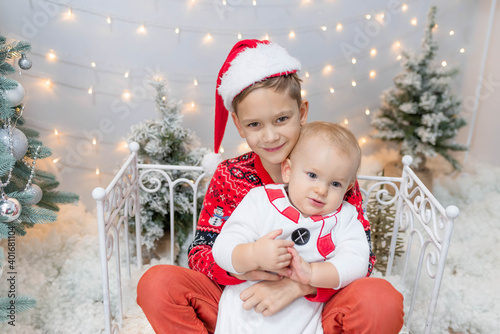 two beautiful brothers in Christmas costumes are sitting by the fence and hugging. friendship of brothers, support, family, holiday, postcard