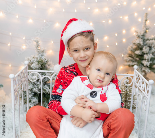 two beautiful little brothers in New Year's costumes are sitting near the fence hugging