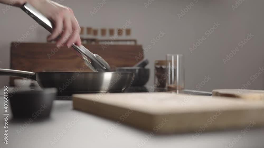 Man flip beef steak with tongs on steel pan on electric hob on kitchen Man flip beef steak with tongs on steel pan on electric hob on kitchen
