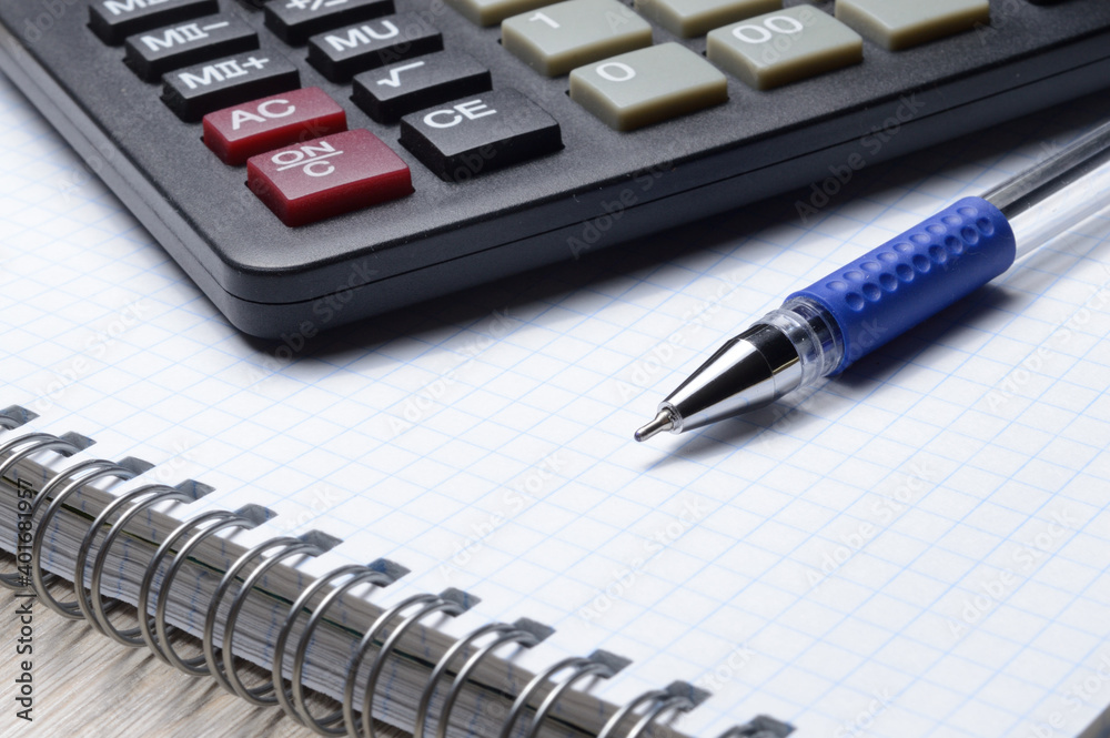 a ballpoint pen and a micro calculator lie on a squared notebook. close-up. a ballpoint pen and a micro calculator lie on a squared notebook. close-up.