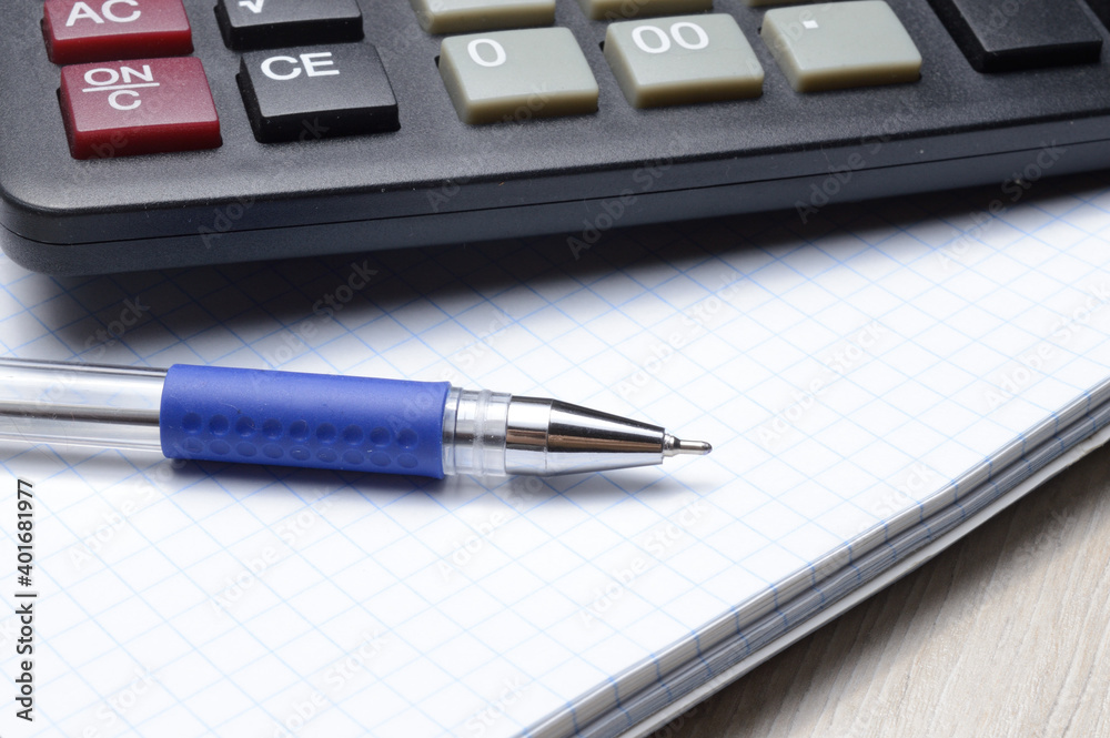 a ballpoint pen and a micro calculator lie on a squared notebook. close-up. a ballpoint pen and a micro calculator lie on a squared notebook. close-up.