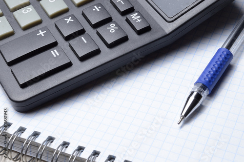 a ballpoint pen and a micro calculator lie on a squared notebook. close-up.