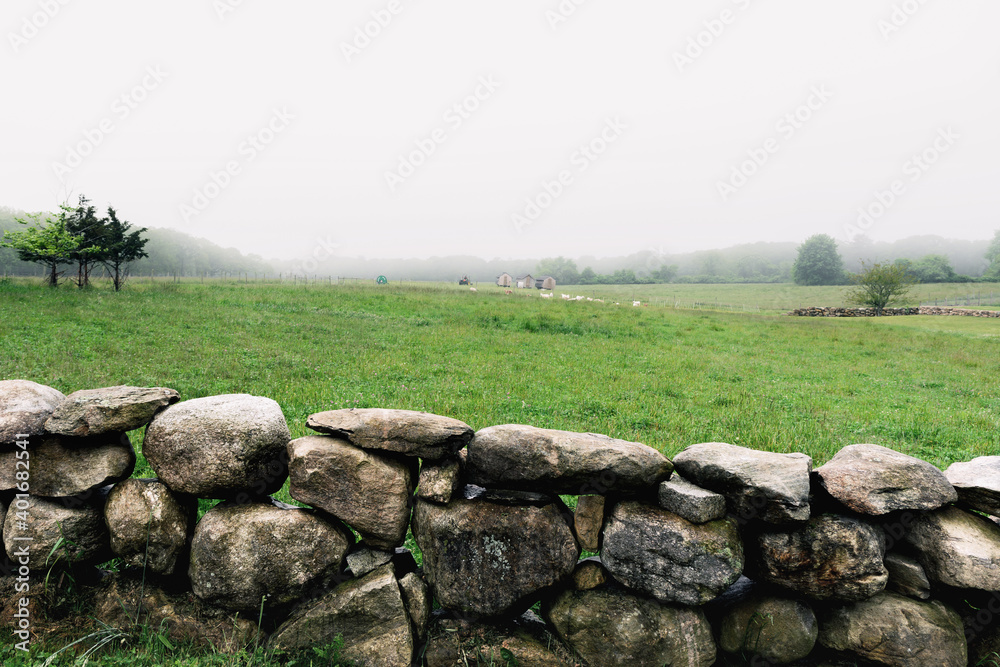 Soft morning fog over an old stone wall with farmland in the background
