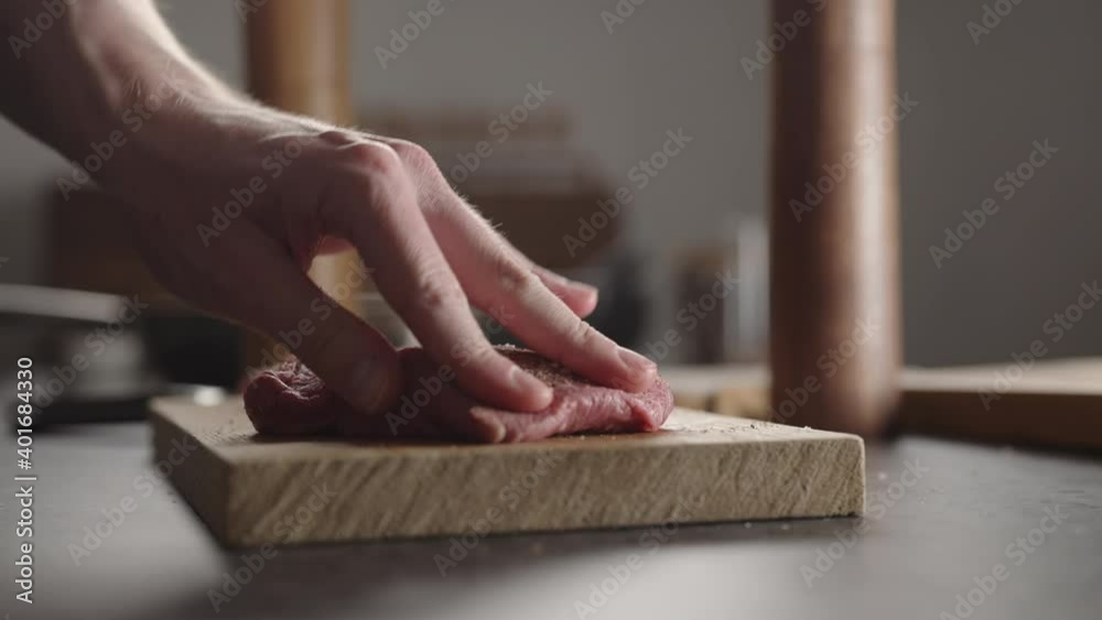 Man seasoning steak with salt and pepper and rolling it over on wood board Man seasoning steak with salt and pepper and rolling it over on wood board