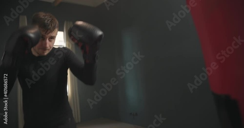 A young athletic man is hitting a boxing bag. Boxer practicing punches in the ring. The athlete strikes with a punching bag. 4k video photo