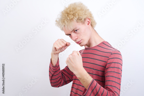 Young handsome Caucasian blond man standing against white background Ready to fight with fist defense gesture, angry and upset face, afraid of problem.