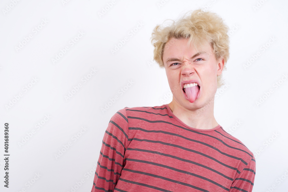Young handsome Caucasian blond man standing against white background sticking tongue out happy with funny expression. Emotion concept. Young handsome Caucasian blond man standing against white background sticking tongue out happy with funny expression. Emotion concept.