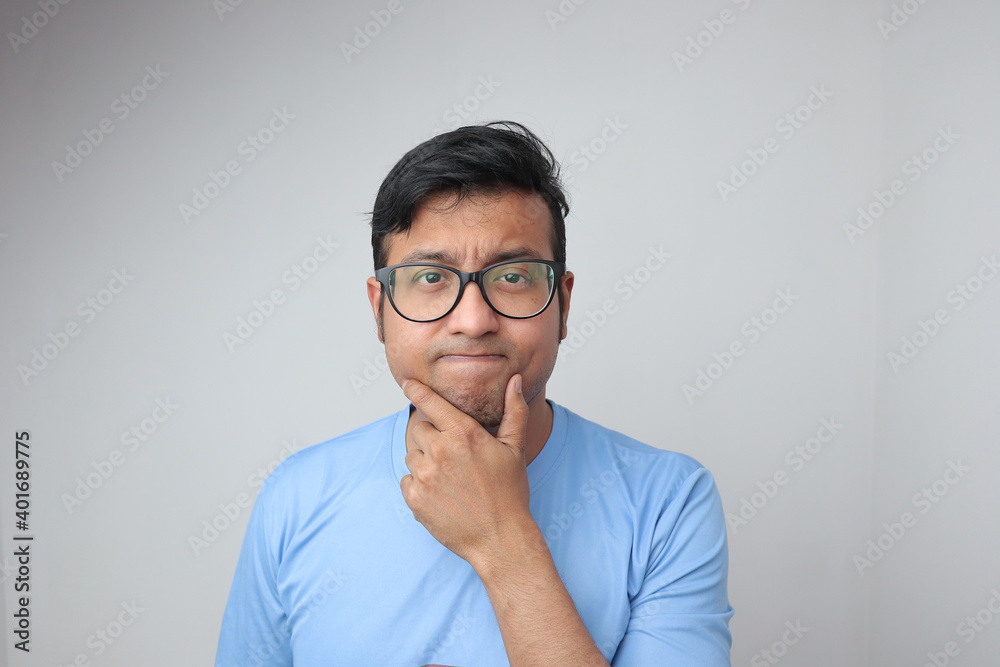 a young indian man in spectacles holding his chin and looking confused and thoughtful a young indian man in spectacles holding his chin and looking confused and thoughtful