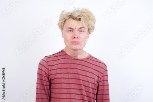 Displeased upset Young handsome Caucasian blond man standing against white background frowns face as going to cry, being discontent and unhappy as can't achieve goals, Disappointed model has troubles