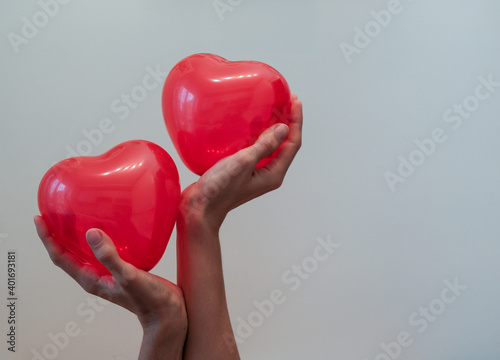 Fototapeta Naklejka Na Ścianę i Meble -  Two female hands hold two red balls in the shape of a heart, on a white background.