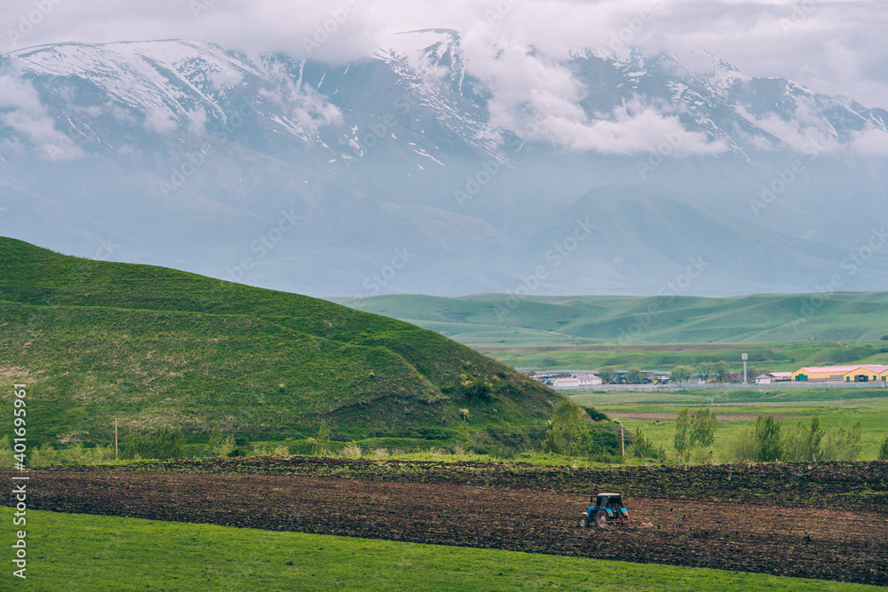Tractor in a green meadow and against the backdrop of a mountain