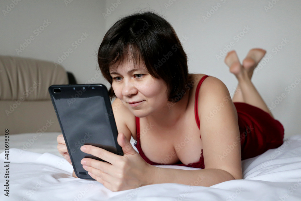 Smiling woman lying with tablet PC on the bed. Concept of online communication, leisure at home Smiling woman lying with tablet PC on the bed. Concept of online communication, leisure at home