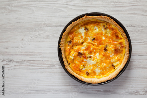 Homemade Bacon Quiche with Eggs and Cheddar Cheese on a white wooden surface, overhead view. Flat lay, from above, top view. Space for text.