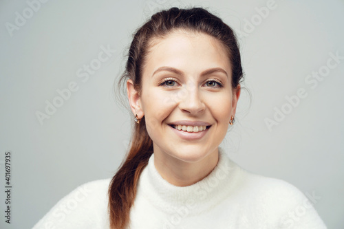 shows a smile cool super young brunette woman with pigtail caucasian appearance. Clothing white fluffy warm stylish jacket. copy space, gray background