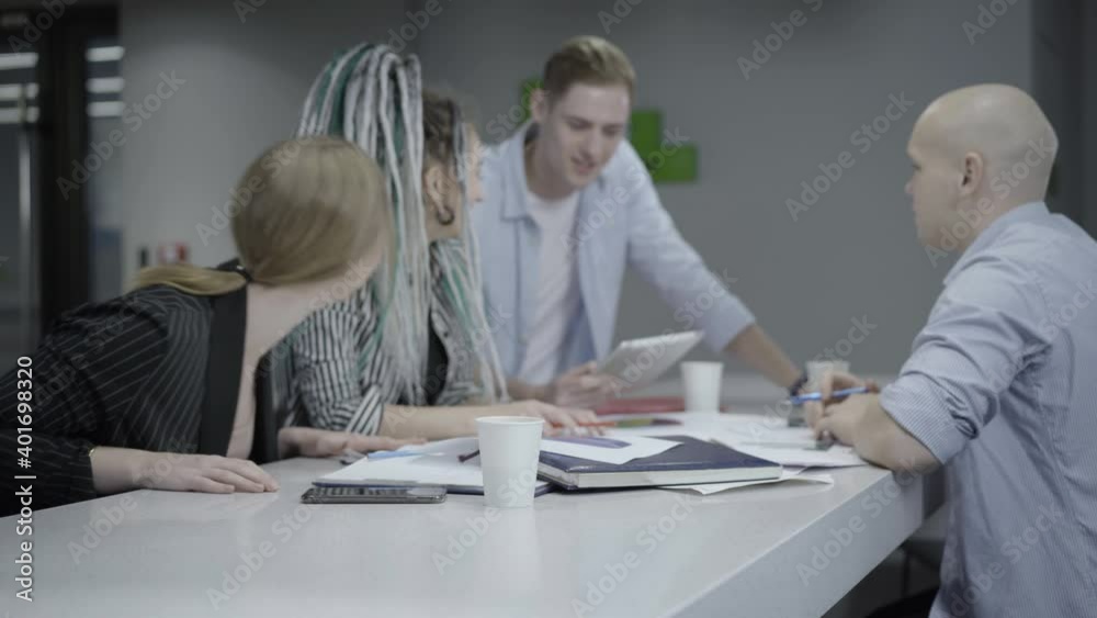 Group of positive coworkers talking and laughing in office. Cheerful young Caucasian men and women discussing project in friendly atmosphere. Teamwork and friendship concept. Group of positive coworkers talking and laughing in office. Cheerful young Caucasian men and women discussing project in friendly atmosphere. Teamwork and friendship concept.