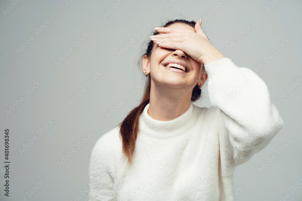 smiling he closed his eyes holding the hand near the face, the gesture funny. young confident female student. Clothing white fluffy warm stylish jacket. copy space smiling he closed his eyes holding the hand near the face, the gesture funny. young confident female student. Clothing white fluffy warm stylish jacket. copy space