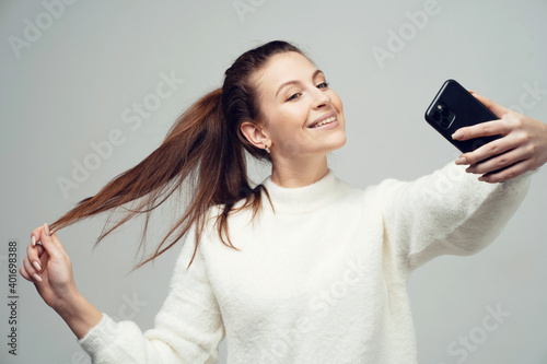 holding the phone makes a selfie photo for parents. young confident female student. Clothing white fluffy warm stylish jacket. copy space