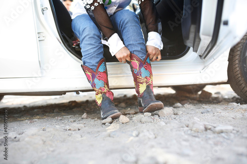 young unrecognizable woman wearing blue jeans with white shirt and putting on cowboy style boots in the car