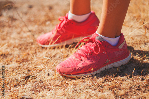 Runner woman legs with pink sneakers is walking on the sunny and yellow grass on a summer day in the evening