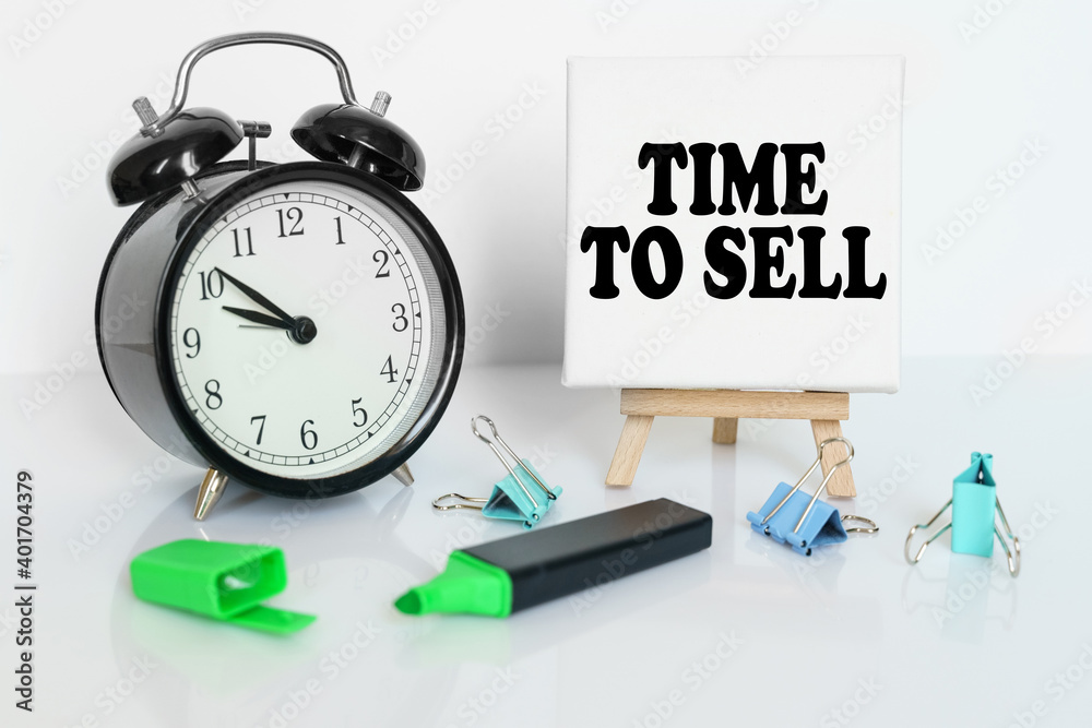 On the table is an alarm clock, a marker and a tripod with a canvas with the inscription - TIME TO SELL On the table is an alarm clock, a marker and a tripod with a canvas with the inscription - TIME TO SELL