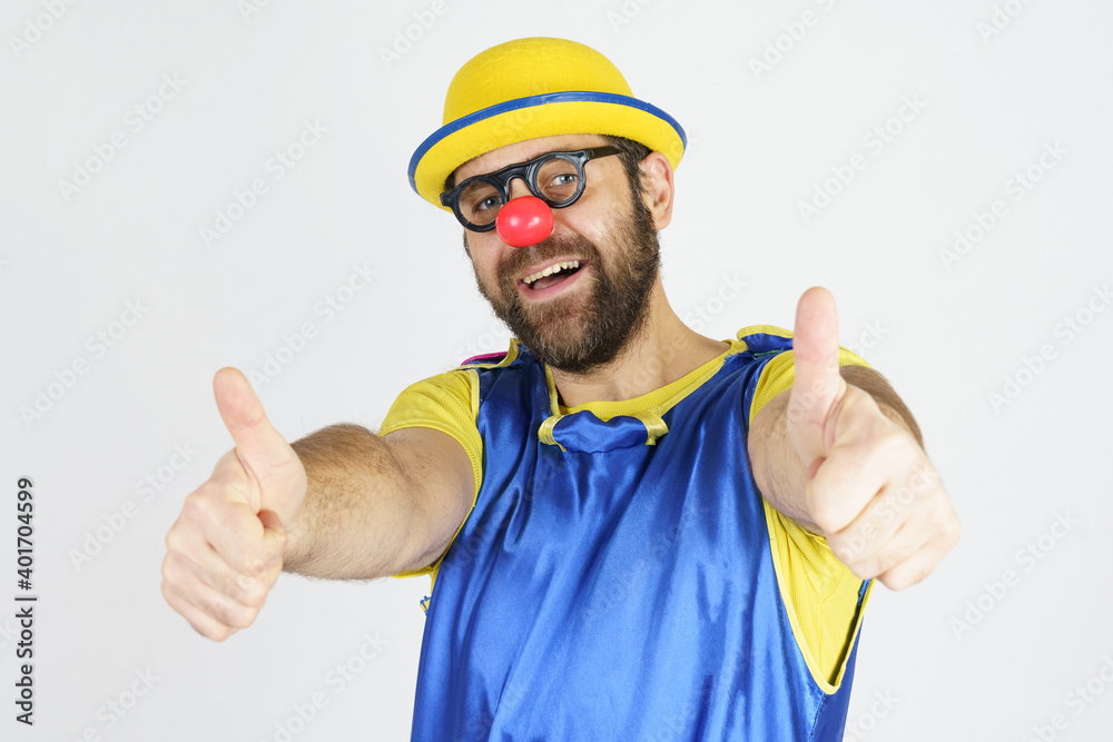 A clown in a bright blue and yellow suit, glasses and a hat shows an OK gesture