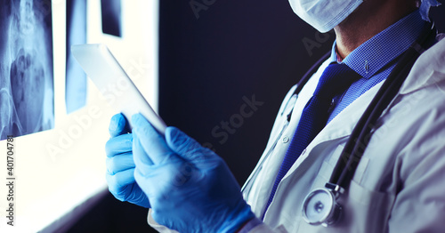 Принти на полотні Doctor in hospital sitting at desk looking at x-rays on tablet against white bac