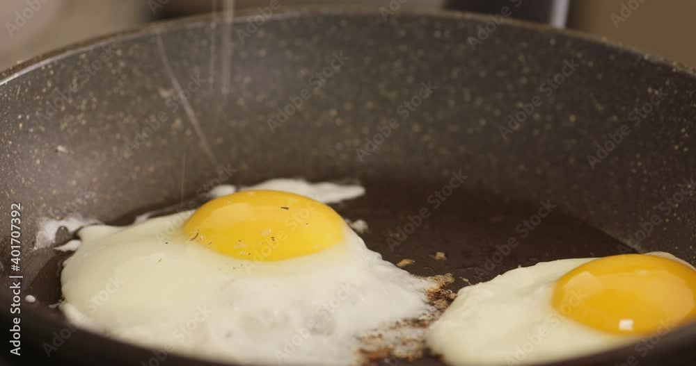 Adding salt and pepper to frying eggs in hot frying pan. Close up. Adding salt and pepper to frying eggs in hot frying pan. Close up.