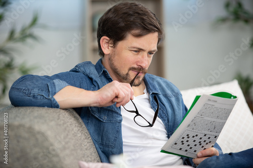 young man sitting doing a crossword puzzle looking thoughtfully photo