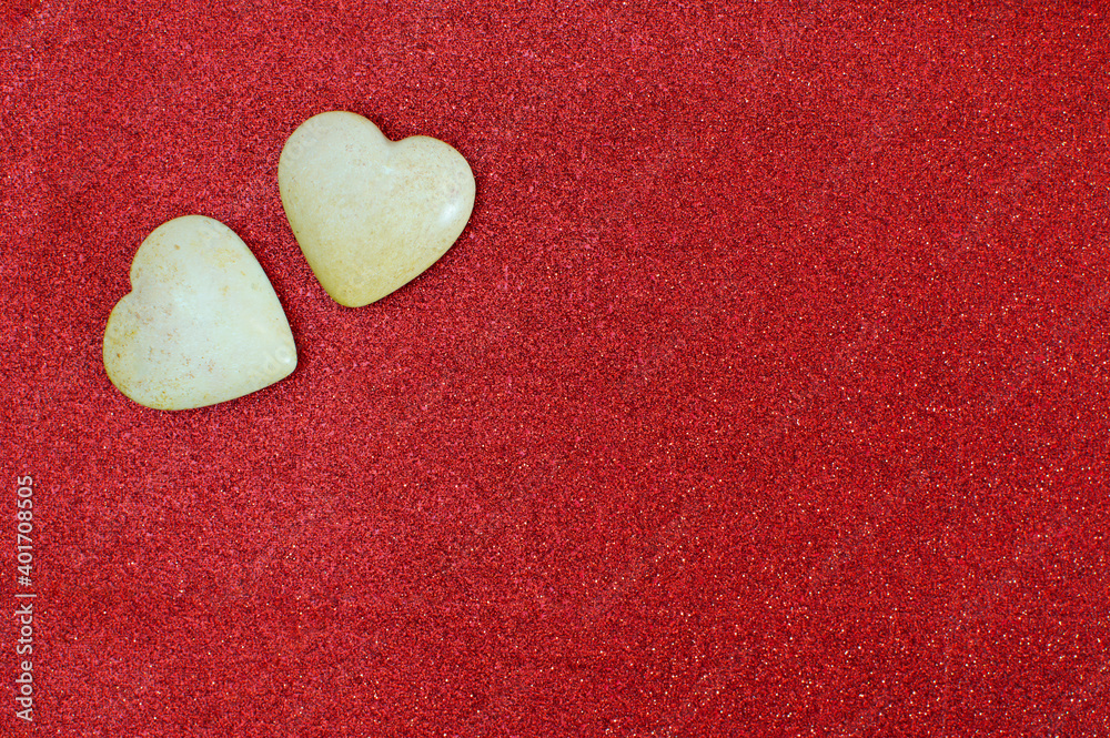 Two polished light stones, carved in the shape of a heart, lie on a beautiful red fabric with sequins. Valentine's holiday symbol, love. Flat lay. Copy space, postcard Two polished light stones, carved in the shape of a heart, lie on a beautiful red fabric with sequins. Valentine's holiday symbol, love. Flat lay. Copy space, postcard