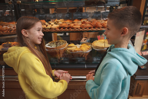 Cute young twin brother and sister smiling at each other near bakery store retail display
