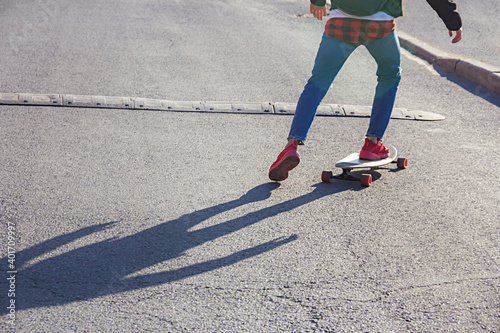 View of legs of a young skateboarder riding on a skateboard approaching the speed bump on a city street road