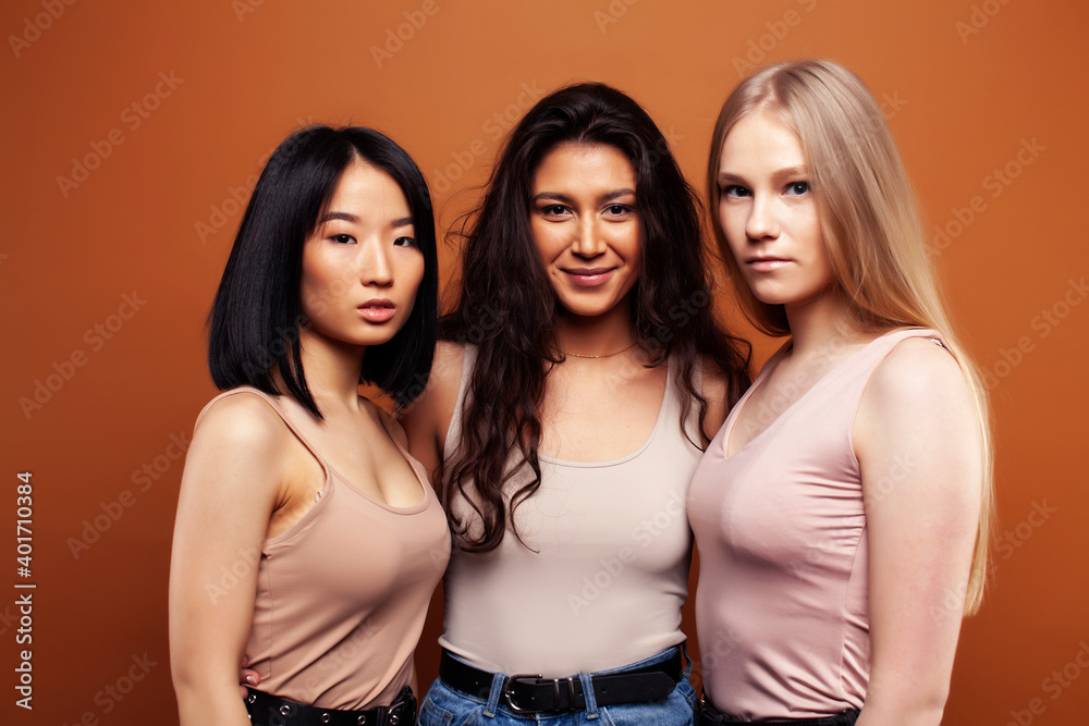 young pretty asian, caucasian, afro woman posing cheerful together on brown background, lifestyle diverse nationality people concept