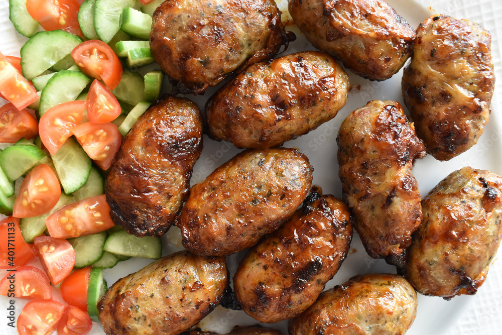 Sheftalia: Cypriot Lamb and Pork Sausages. Grilled Sausages with Fresh Vegetables (Cucumber and Tomato) on a White Plate. Traditional Cypriot food.	
