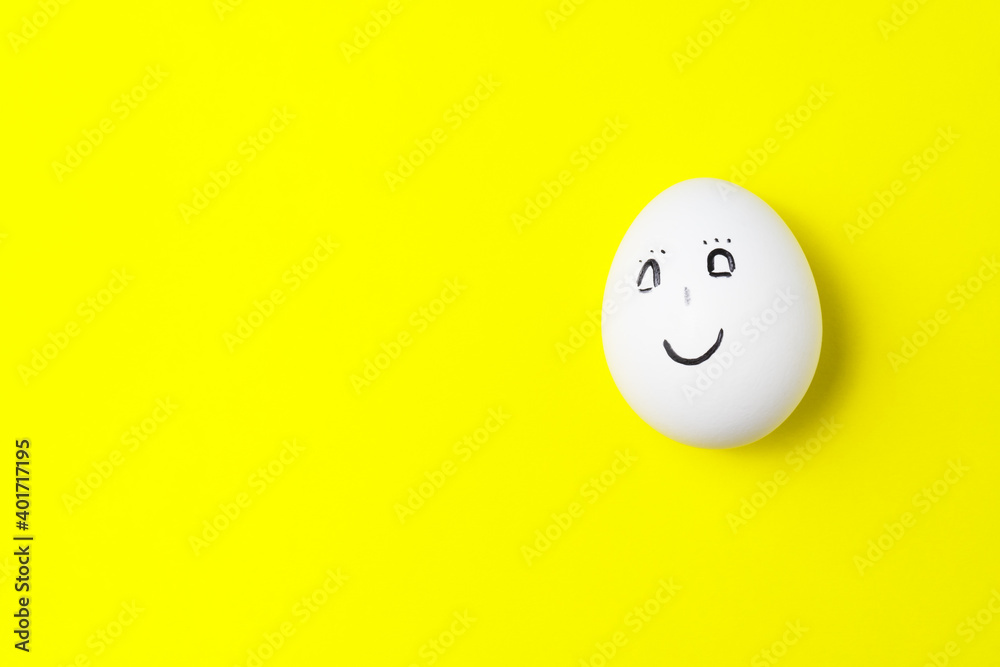 One white chicken egg with smiling face on yellow background with copy space. One white chicken egg with smiling face on yellow background with copy space.