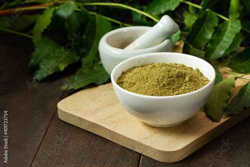 Photos neem powder in white bowl with neem leaf and white mortar and pestle on wooden background