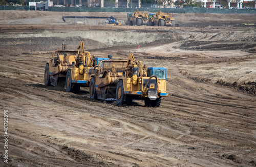 Heavy earthmoving equipment including scapers and motor graders involved in grading operations at a construction site photo