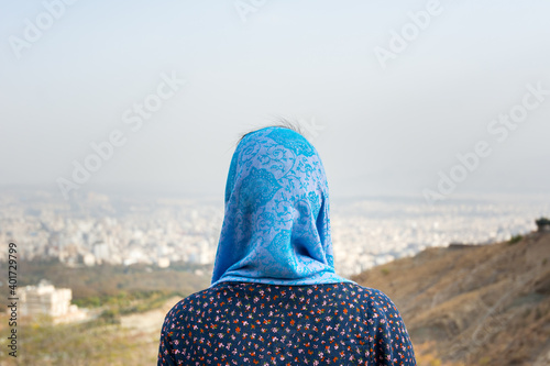 A young Muslim girl wearing blue Hijab and traditional clothes and looking at the city of Tehran from the tochal mountain
