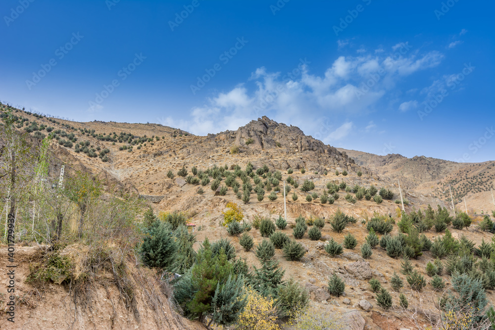 Tochal mountain with rocks and trees in the Zafaraniyeh and velenjak valley gainst blue sky, Tehran, Iran.