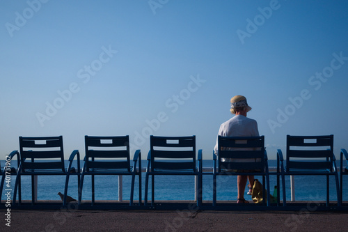 A closeup shot of a person sitting on a blue chair on the beach, a bird under one of the chairs