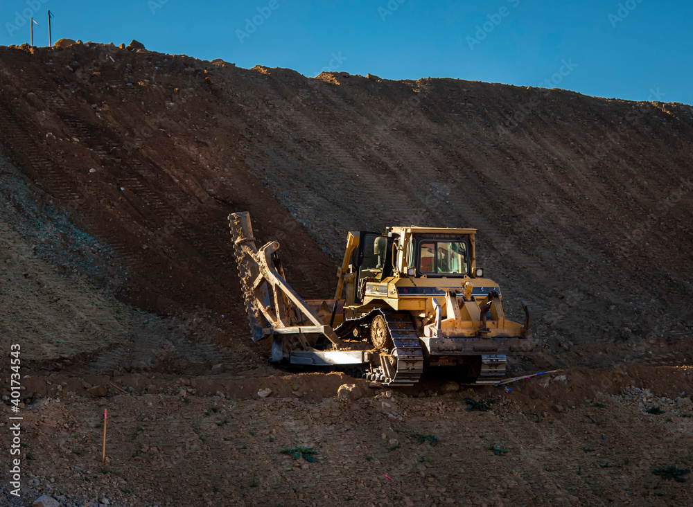 Bulldozer with a single shank ripper on a steep hill at a construction site