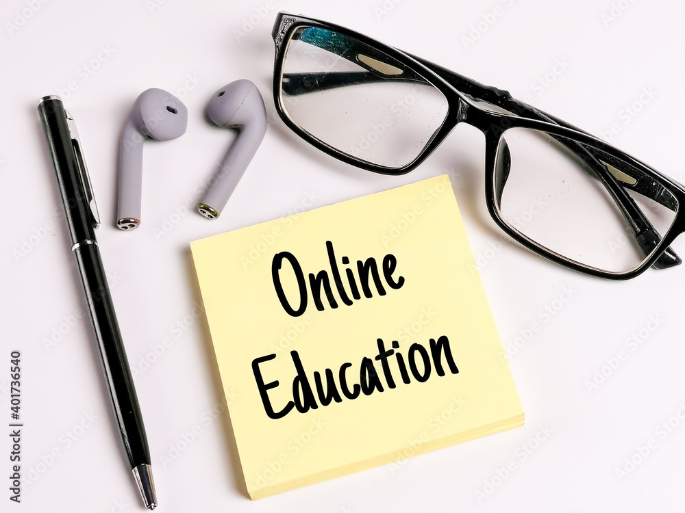 Phrase online education on yellow note paper with a pen,ear buds and eye glasses isolated on white background.Education and business concept.New normal. Phrase online education on yellow note paper with a pen,ear buds and eye glasses isolated on white background.Education and business concept.New normal.