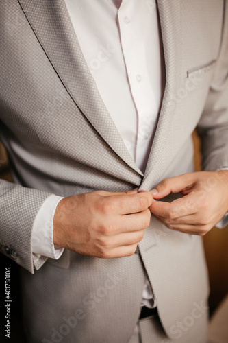 The groom buttons his jacket