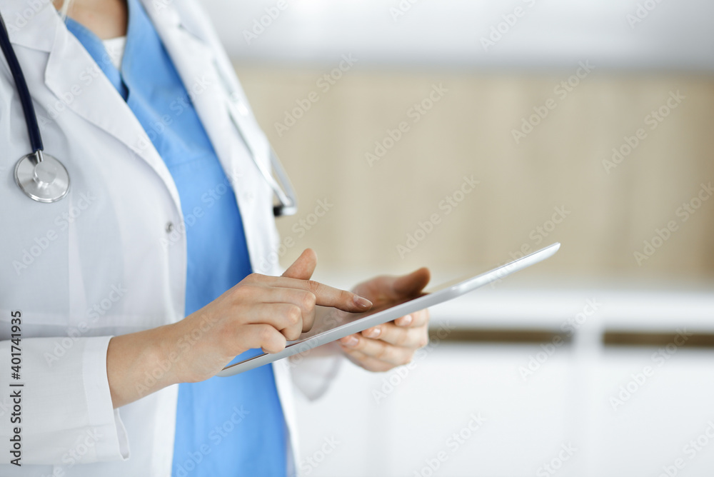 Unknown woman-doctor standing in clinic and using tablet pc, close-up. Data in medicine and healthcare Unknown woman-doctor standing in clinic and using tablet pc, close-up. Data in medicine and healthcare